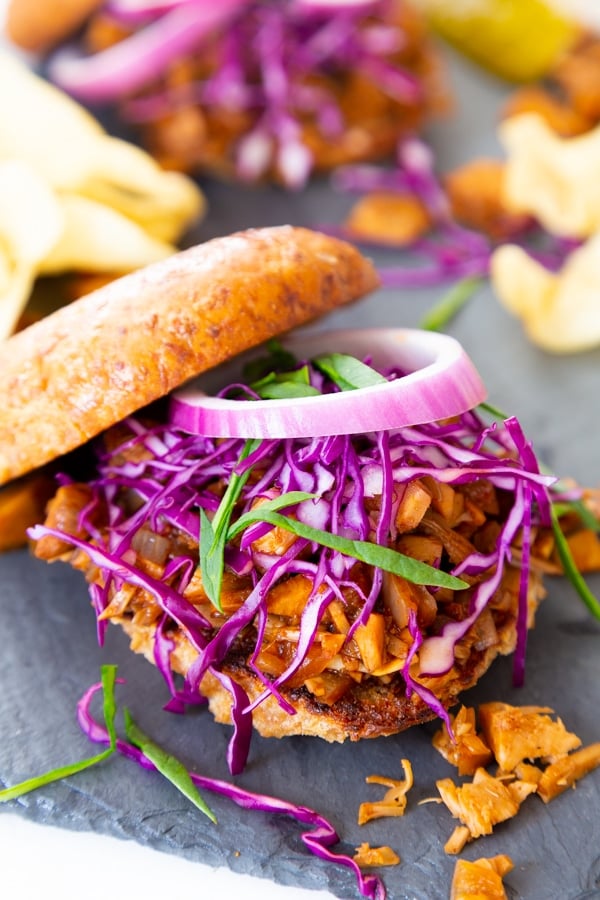 A pulled BBQ sandwich with the bun half on the top and onions and slaw on top of the sandwich