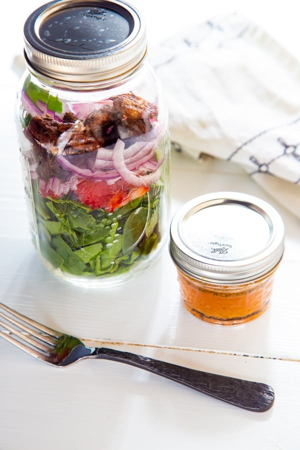 A mason jar with strawberry spinach salad and a jar of dressing and a fork