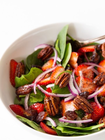 A white bowl with strawberry spinach salad and candied pecans