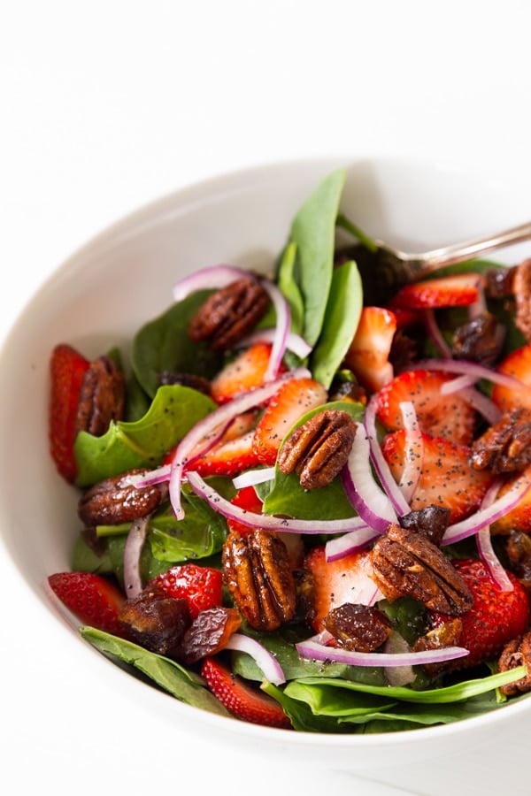 A white bowl with strawberry spinach salad and candied pecans