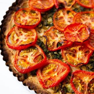Half of a tomato tart in a tart pan on a white surface