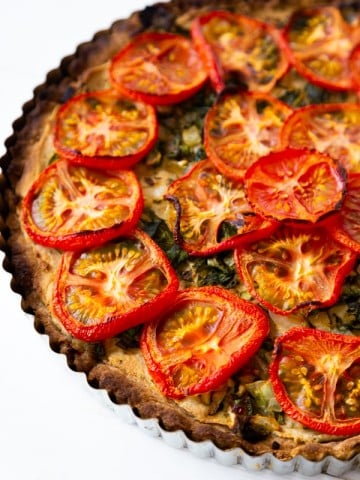 Half of a tomato tart in a tart pan on a white surface