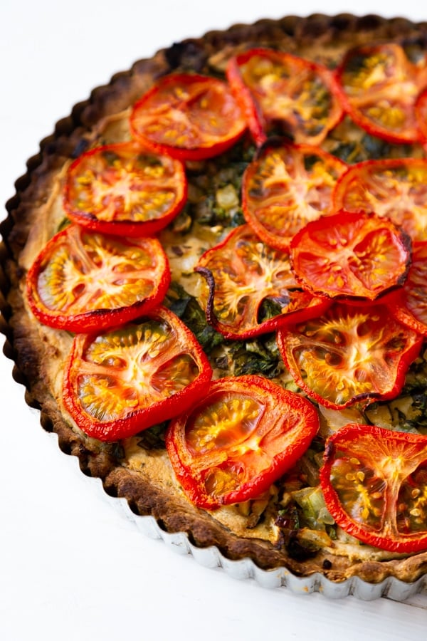 Half of a tomato tart in a tart pan on a white surface