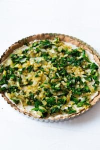 Onion and spinach spread over a tart in a tart pan