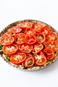 An uncooked tomato tart on a white surface