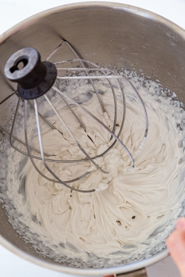 Coconut milk in a silver mixing bowl being whipped into whipped cream with a wire whisk.