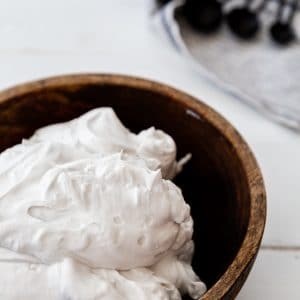 Whipped coconut cream in a wood bowl with a towel next to it.