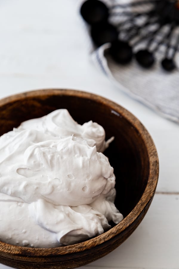 Whipped coconut cream in a wood bowl with a towel next to it. 