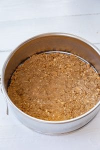 vegan cheesecake crust ingredients pressed into a springform pan on a white board