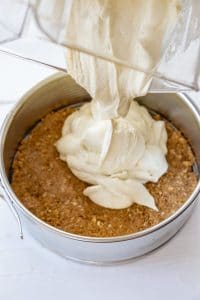 vegan cheesecake filling being poured over the crust in the springform pan on a white board