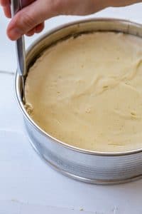 vegan cheesecake in a springform pan being cut away from the sides on a white board