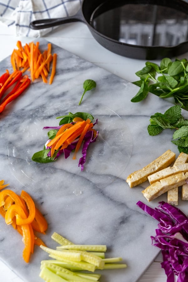 Rice paper with carrots and other vegetables on top of it on a marble board.