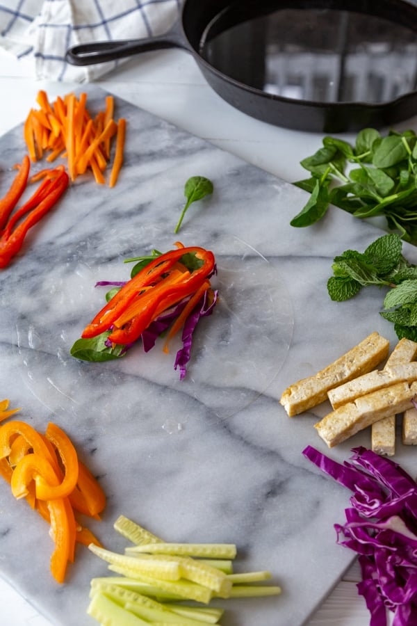 Rice paper on a marble board with bell pepper matchsticks and other vegetables on top of it.