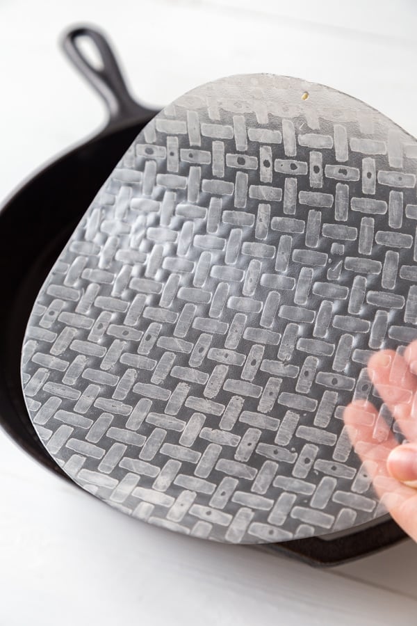 A round piece of rice paper being dipped into a pan of water. 