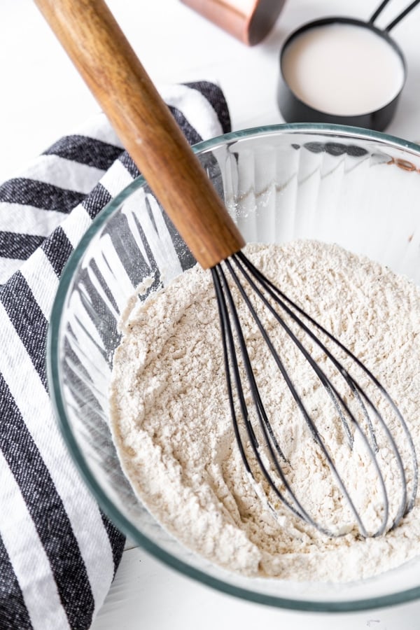 A glass bowl with flour and spices and a wooden whisk in the bowl.