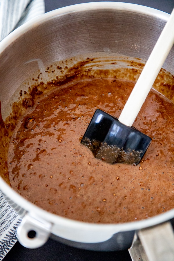 A silver mixing bowl with chocolate cake batter and a spatula stirring the batter.