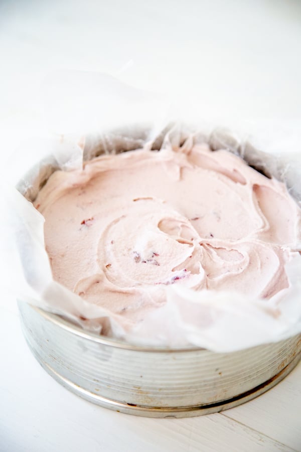 A silver springform pan lined with wax paper and filled with cherry ice cream.