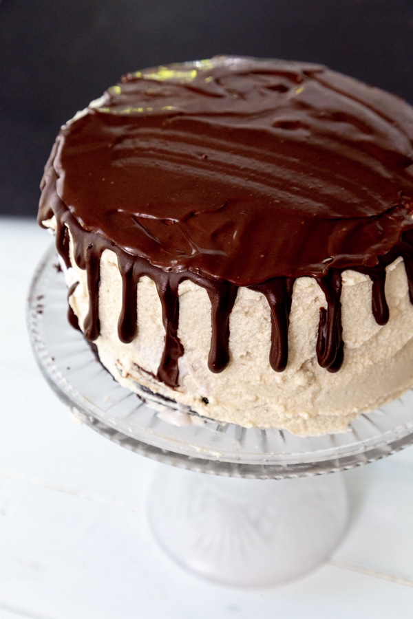 A cake with vanilla frosting and chocolate ganache dripping down the sides and on the top of the cake.