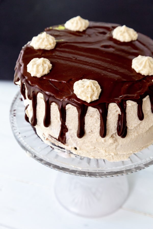 A cake with vanilla frosting and chocolate ganache on the top and dripping down the sides with dollops of frosting around the edge of the cake.
