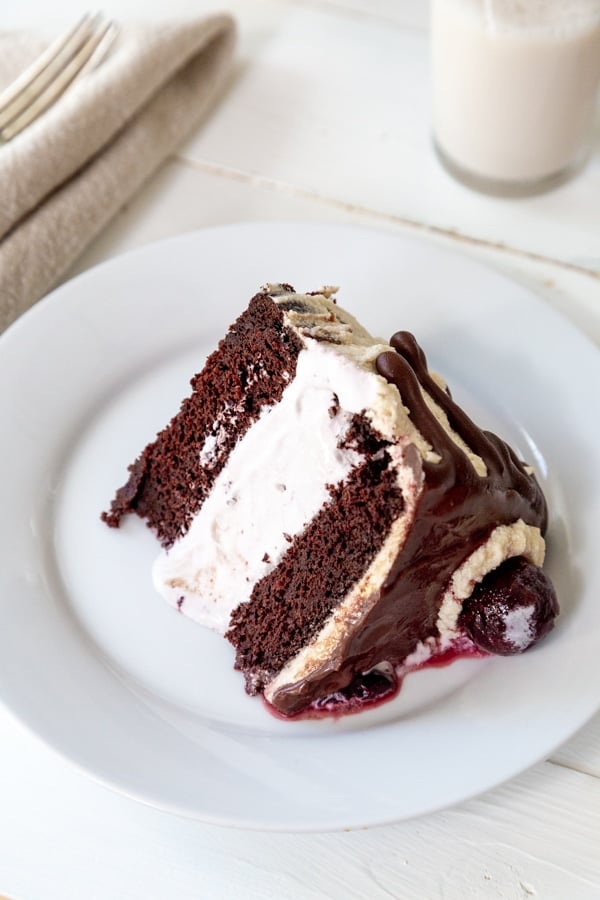 A slice of chocolate and cherry ice cream cake on a white plate with a glass of milk in the background.