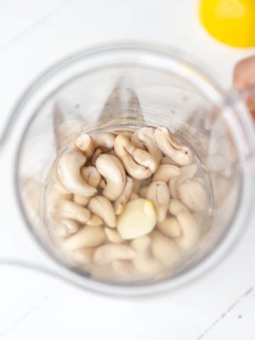 An overhead shot of cashews in a blender with a lemon on the side.