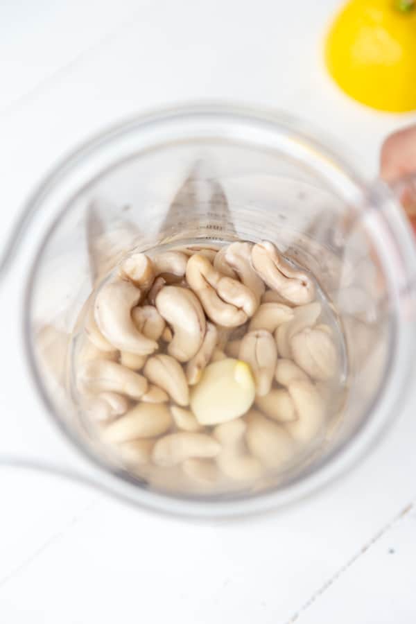 An overhead shot of cashews in a blender with a lemon on the side.