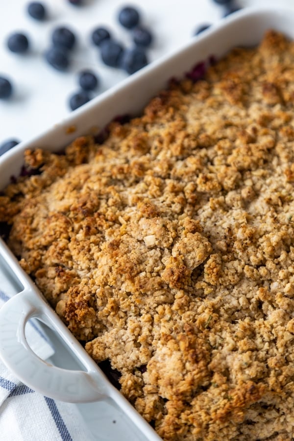 A pan of blueberry crisp with blueberries scattered on the table next to it.