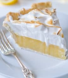 A slice of lemon meringue pie on a white plate with a silver fork resting on the plate.