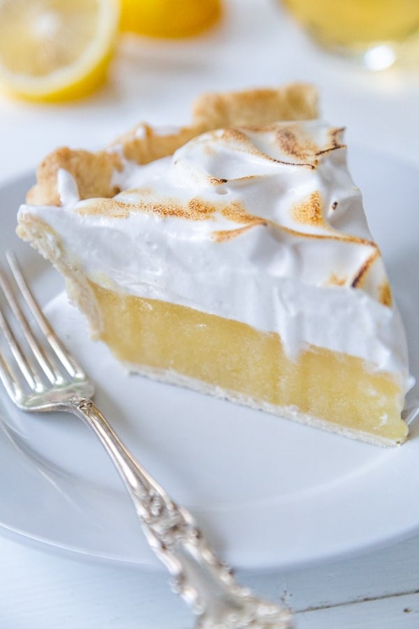 A slice of lemon meringue pie on a white plate with a silver fork resting on the plate.