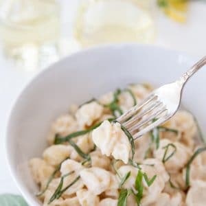 A white bowl of pasta with cream sauce and ribbons of basil with a gold fork in the bowl.
