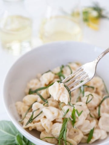 A white bowl of pasta with cream sauce and ribbons of basil with a gold fork in the bowl.