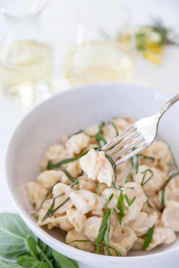 A white bowl of pasta with cream sauce and ribbons of basil with a gold fork in the bowl.