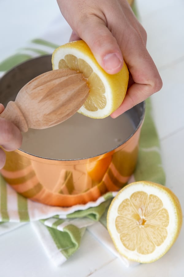 A hand squeezing lemon juice from a lemon with a wood juicer into a copper pan.