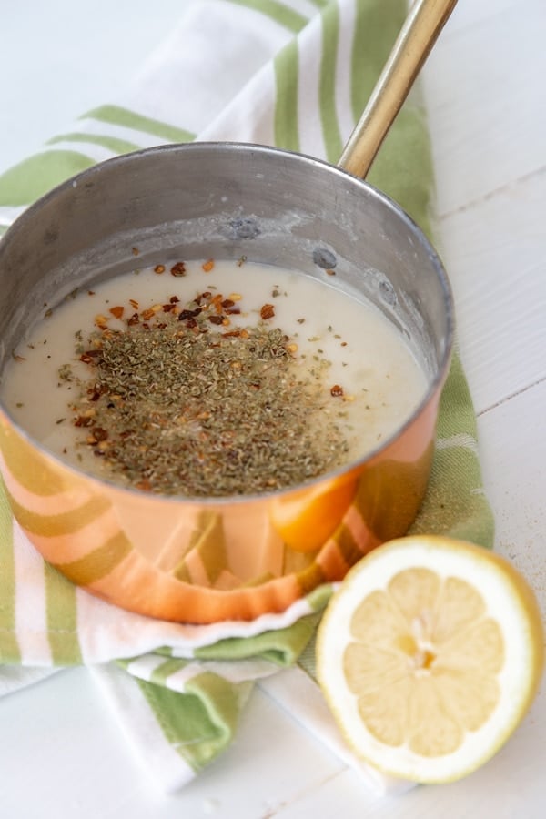 A cream sauce with spices in a copper pan with a half of a lemon next to it.