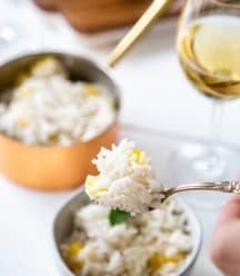 A hand holding a fork with mango rice over a bowl of rice and a copper pot of rice and a glass of wine in the background.