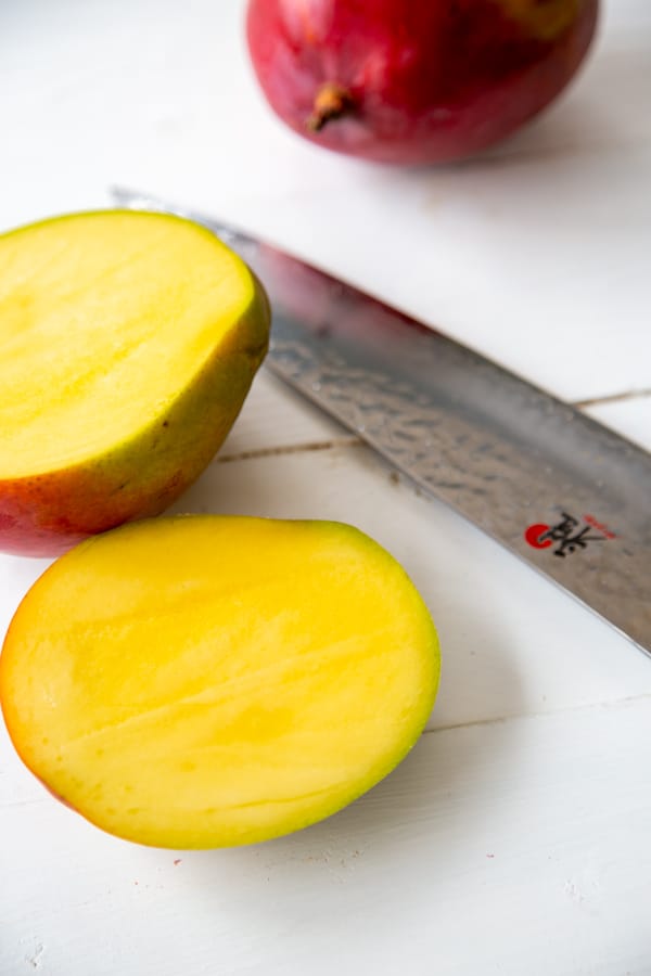 A mango sliced in half with a knife on a white table.