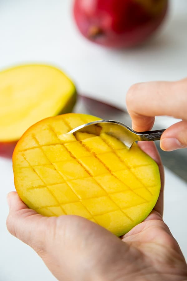 A hand with a spoon scooping out sliced mango.