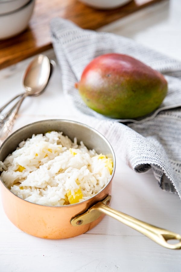 A copper pot with rice and a mango and spoon next to it.