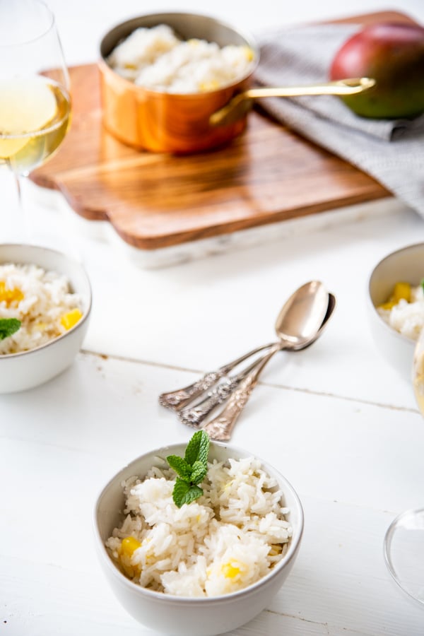 A tablescape with white bowls with mango rice and a copper pot of rice.