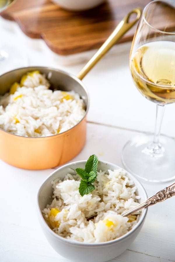 A bowl of coconut mango rice with a copper pot of rice and a board with mango int he background