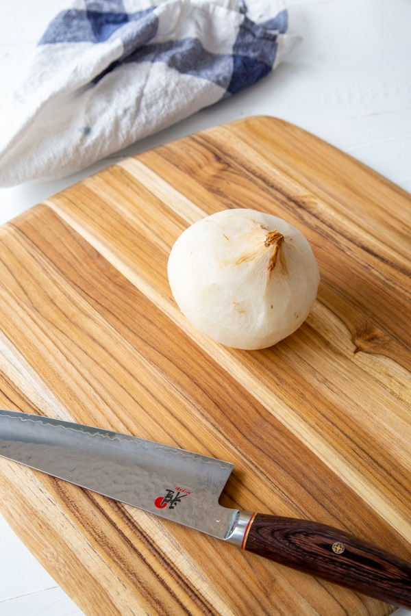 A whole peeled jicama on a wood board with a knife.