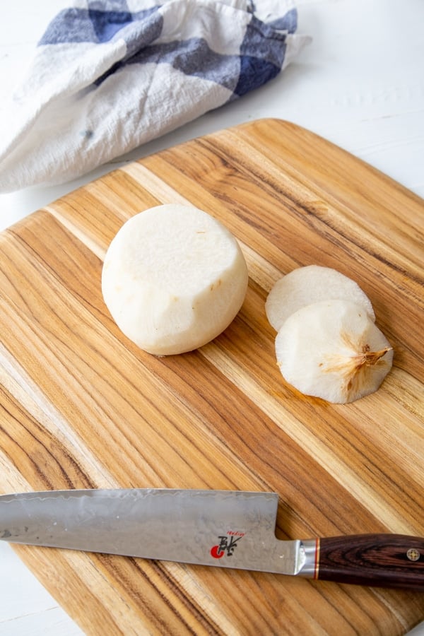 A peeled jicama cut in half on a wood board with a knife.