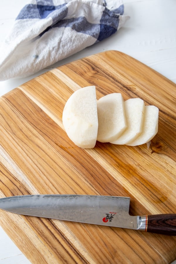 A jicama sliced into pieces on a cutting board with a knife.