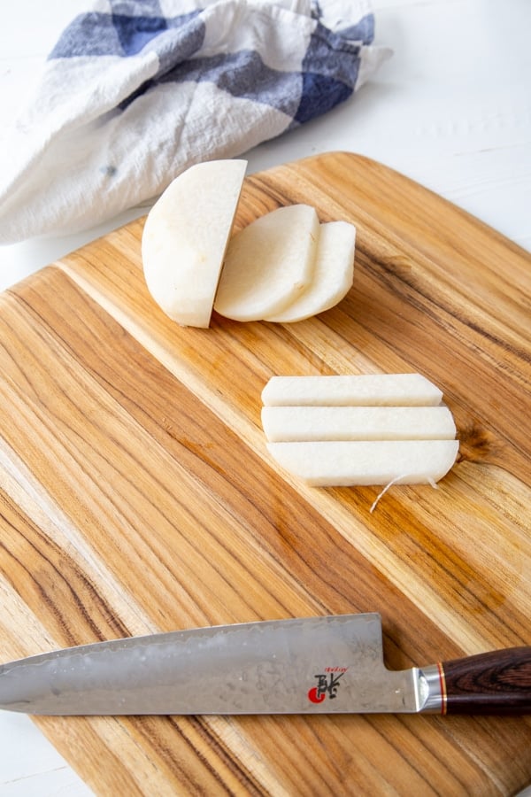 A sliced jicama with one piece sliced into sticks on a wood cutting board.