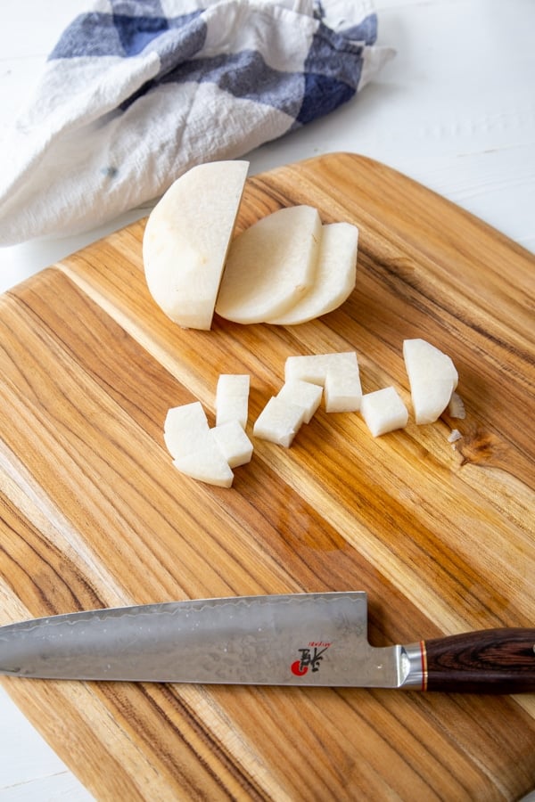 A sliced jicama with cubed pieces next to it on a wood board with a knife.