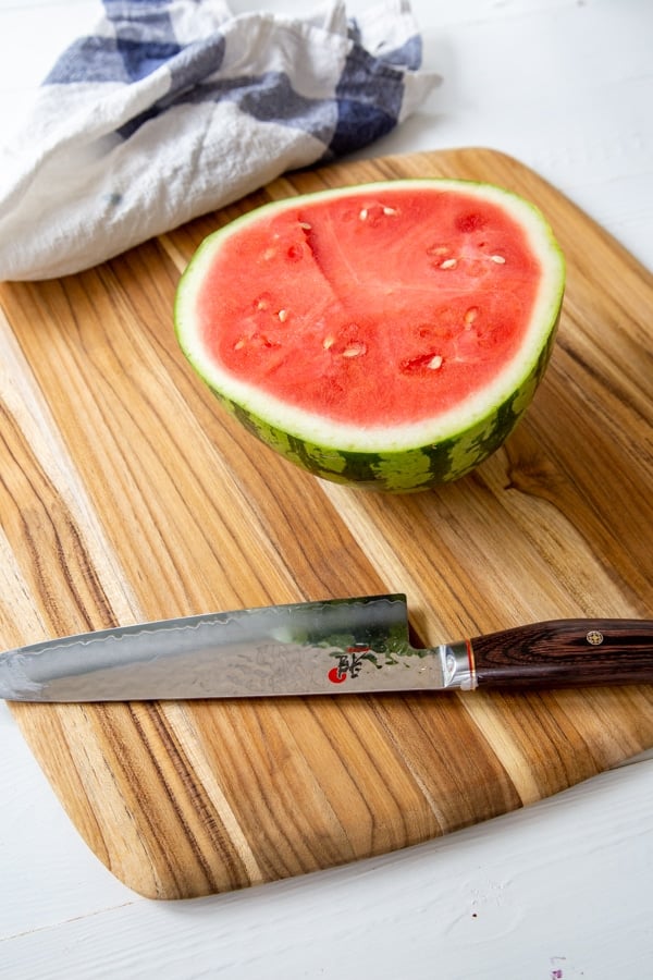 Half of a watermelon on a wood board with a knife next to it.