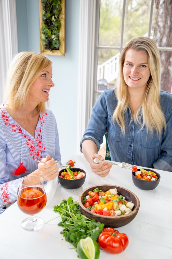 Two blonde women smiling and eating salads at a white table.