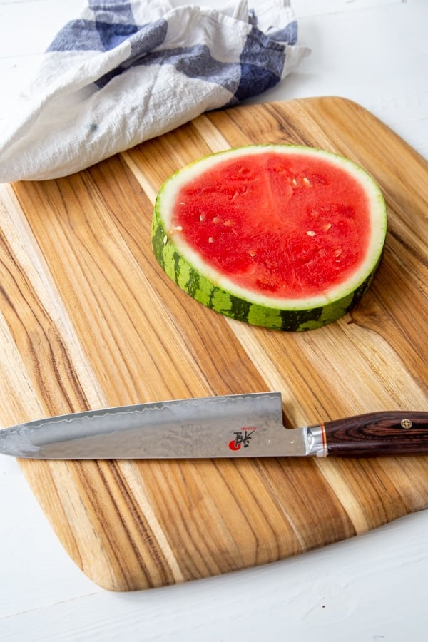 A whole slice of watermelon on a board with a knife next to it.