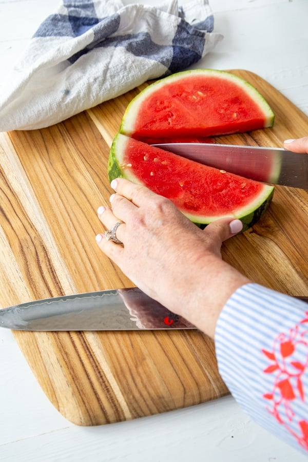 A woman's hand holding half of a watermelon and slicing it in the center with a knife.