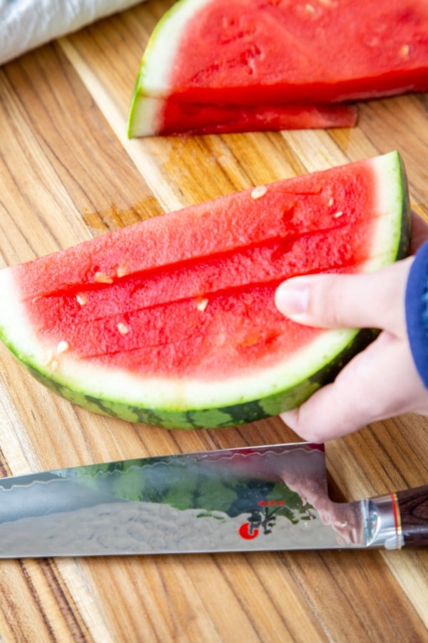 A hand holding a sliced half of watermelon.